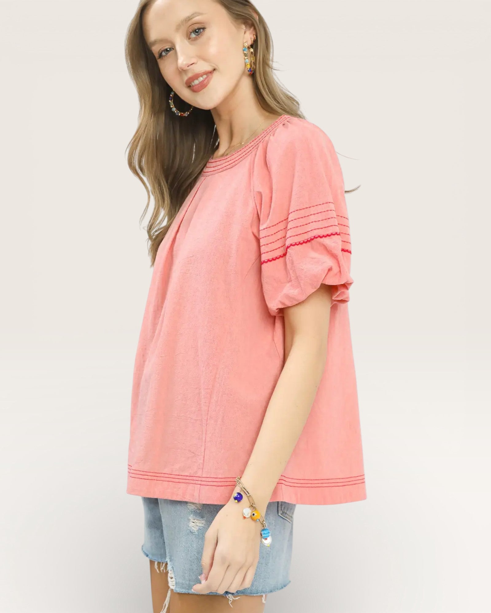 Woman wearing a pink top and denim shorts on a plain background