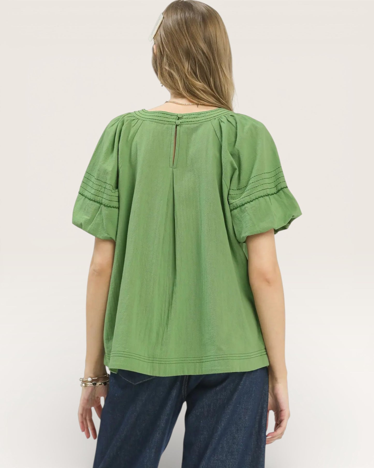 Person wearing a green blouse with ruffled sleeves on a white background