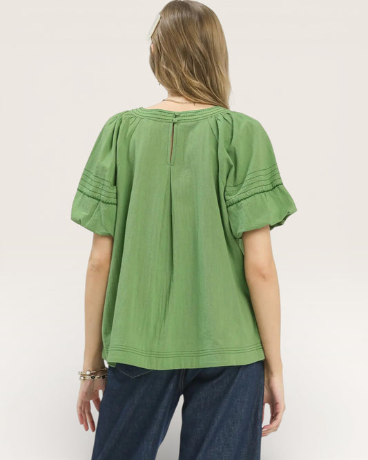 Person wearing a green blouse with ruffled sleeves on a white background