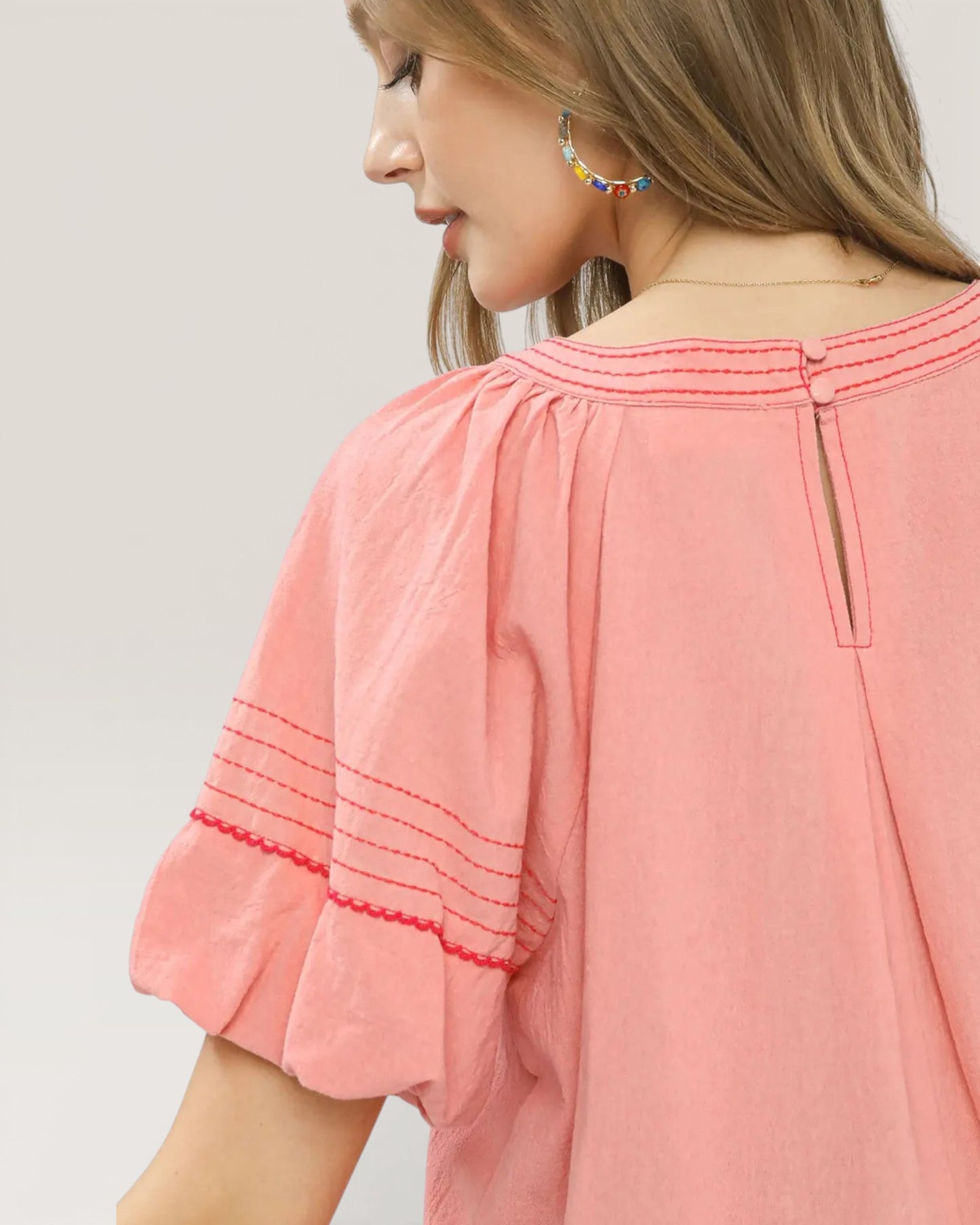 Woman wearing a pink blouse with embroidered details on a plain background