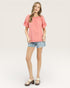 Woman wearing a coral top and denim shorts on a white background
