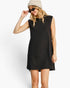 A woman modeling a black sleeveless mini dress with a relaxed, oversized fit, styled with a beige knit beanie and sunglasses against a plain white studio background.