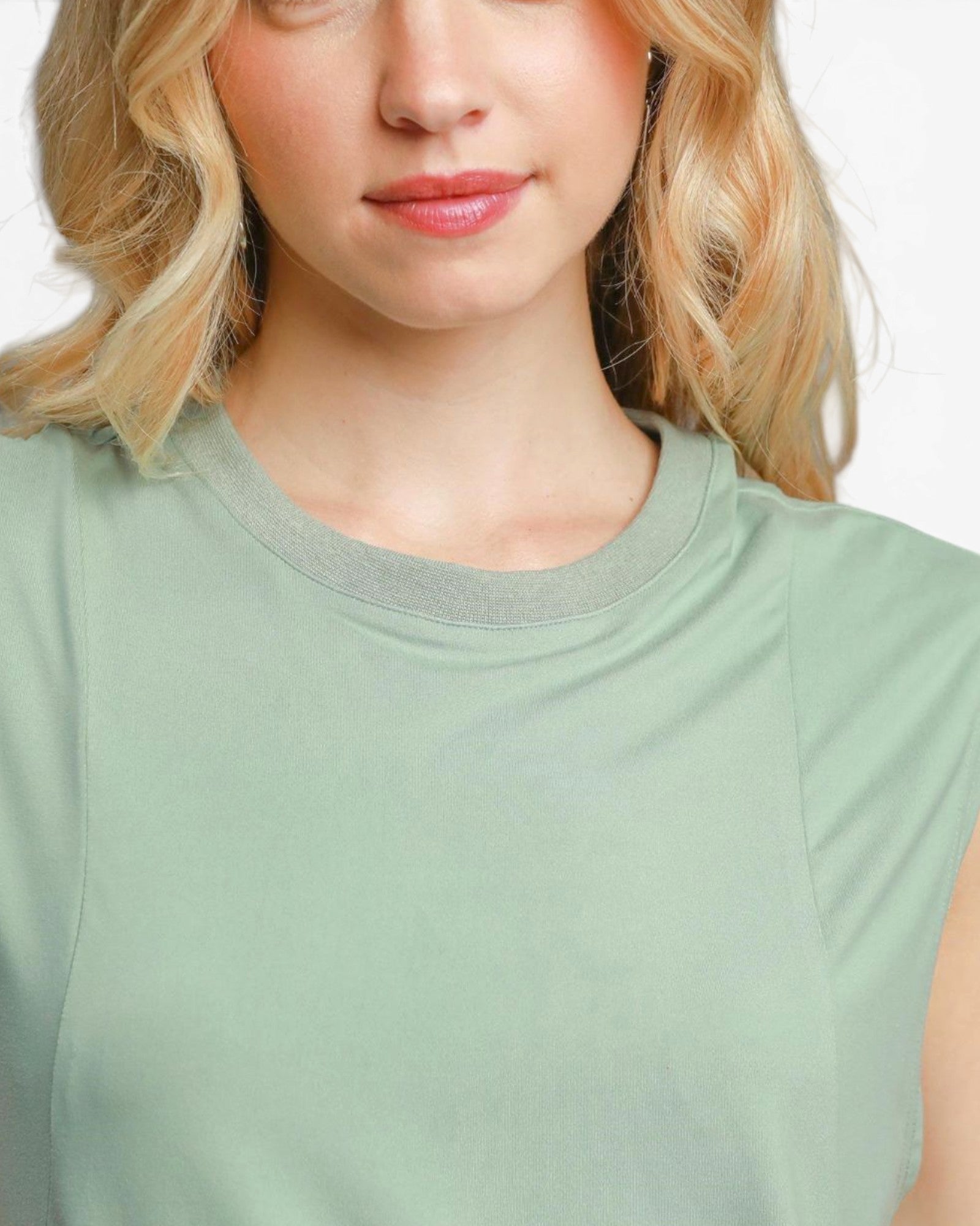 Close-up of a woman wearing a light sage green sleeveless top with a contrasting gray crew neck trim, shown against a plain white background.
