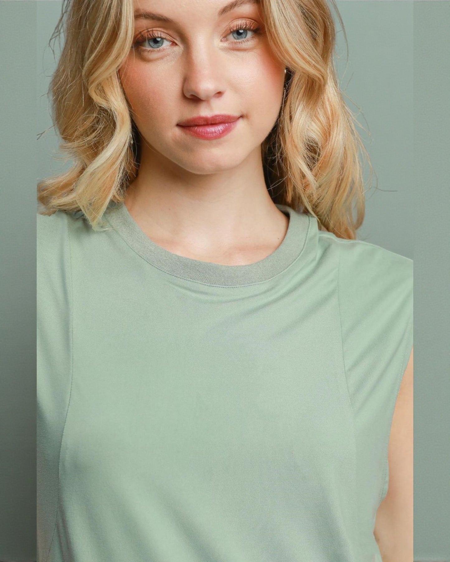 Woman wearing a light green sleeveless top against a plain background