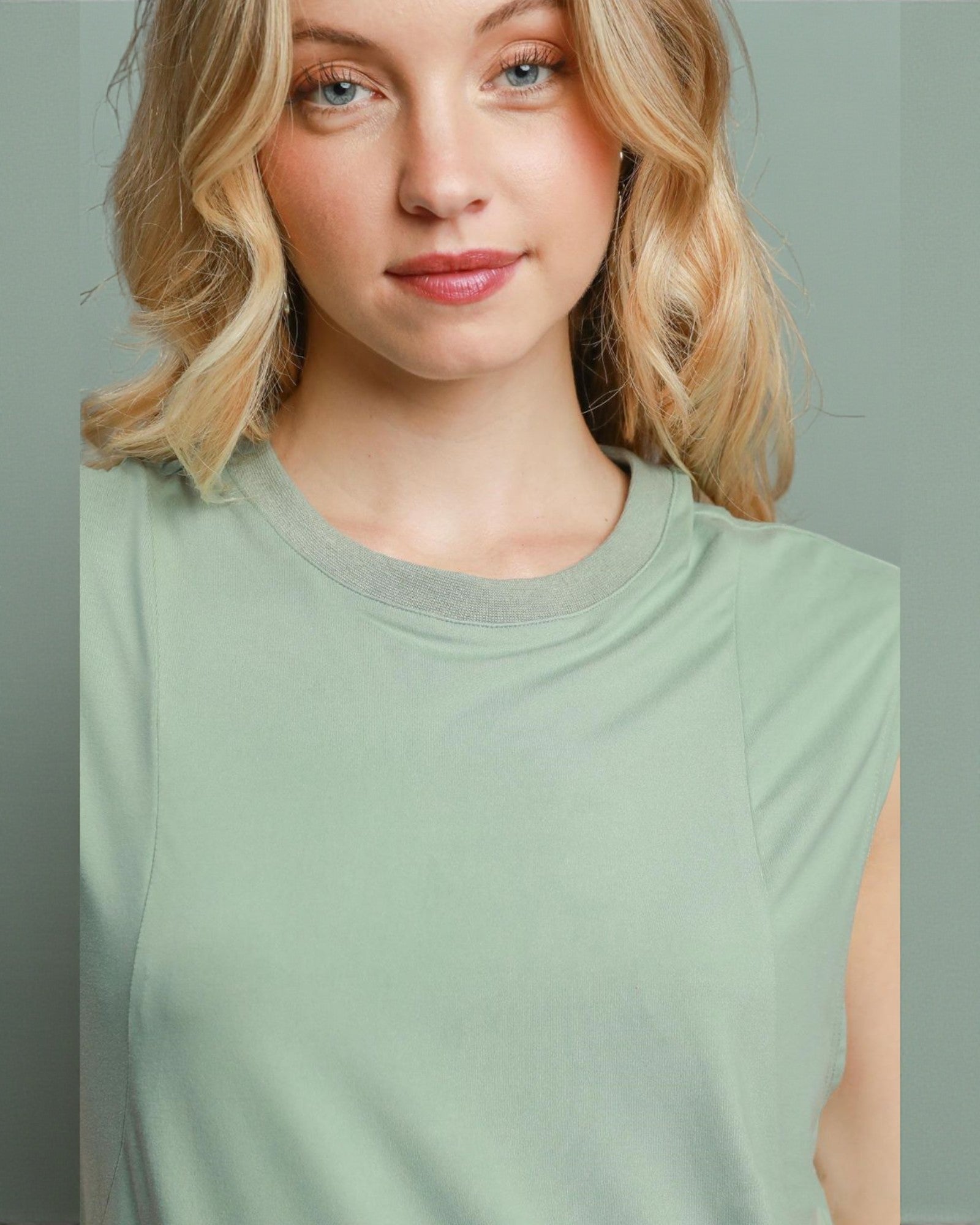Woman wearing a light green sleeveless top against a plain background