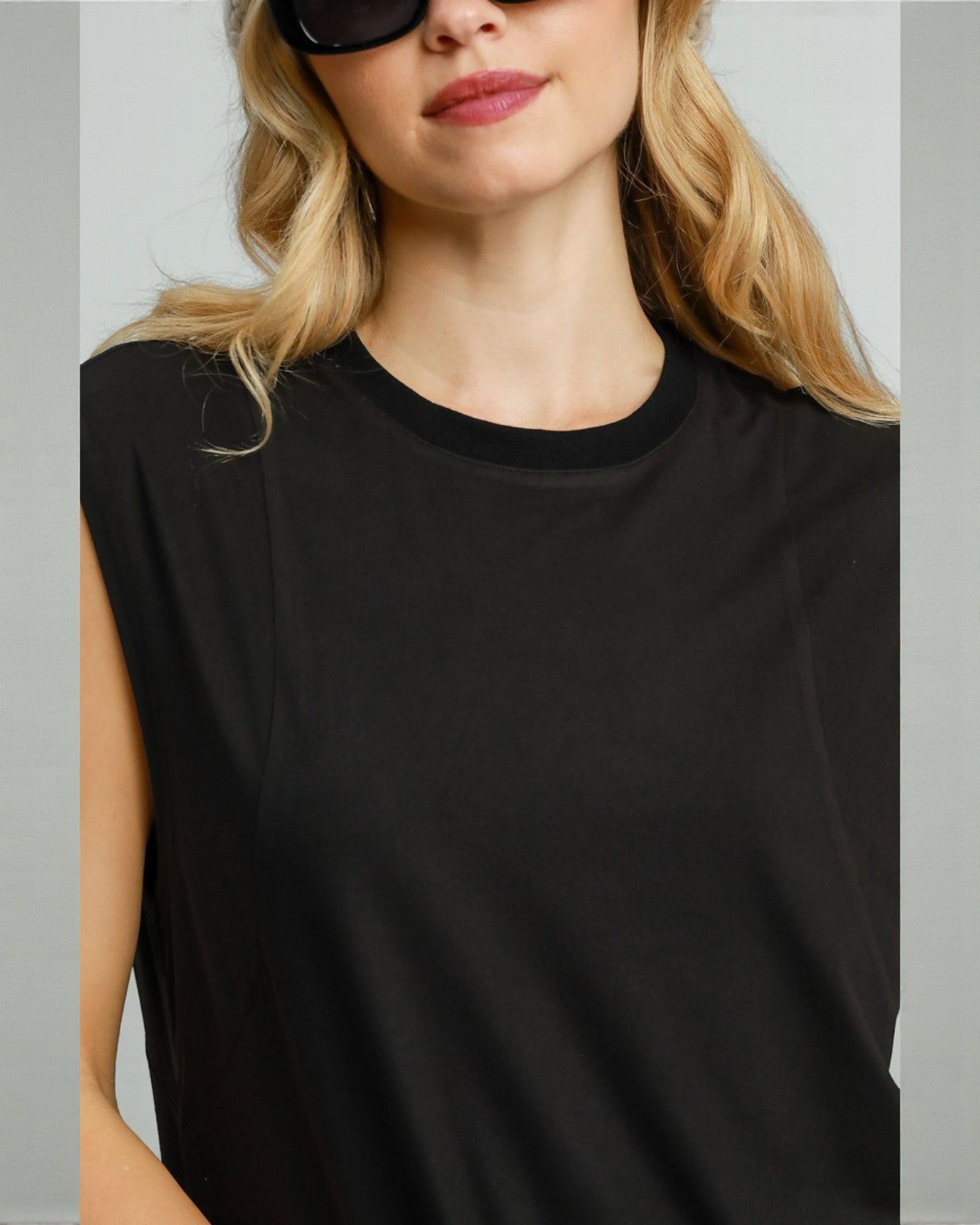 Person wearing a black sleeveless top against a neutral background