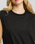 Close-up of a woman wearing a black sleeveless top with a ribbed crew neck, showing her blonde hair and shoulder against a light gray background.