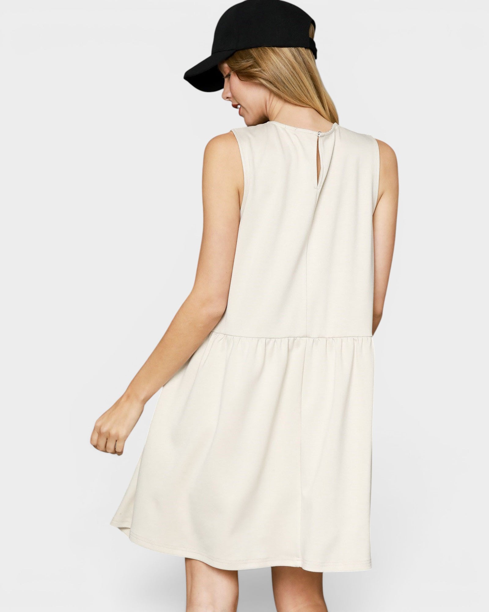 Woman wearing a white dress and black cap on a plain background