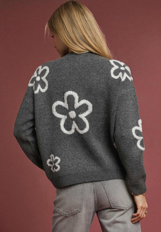 Person wearing a gray sweater with white floral patterns on a red background