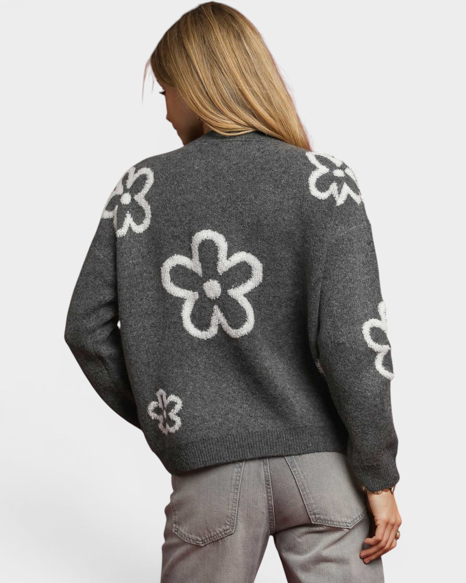 Person wearing a gray sweater with white floral patterns on a plain background