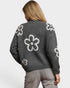 Person wearing a gray sweater with white floral patterns on a plain background