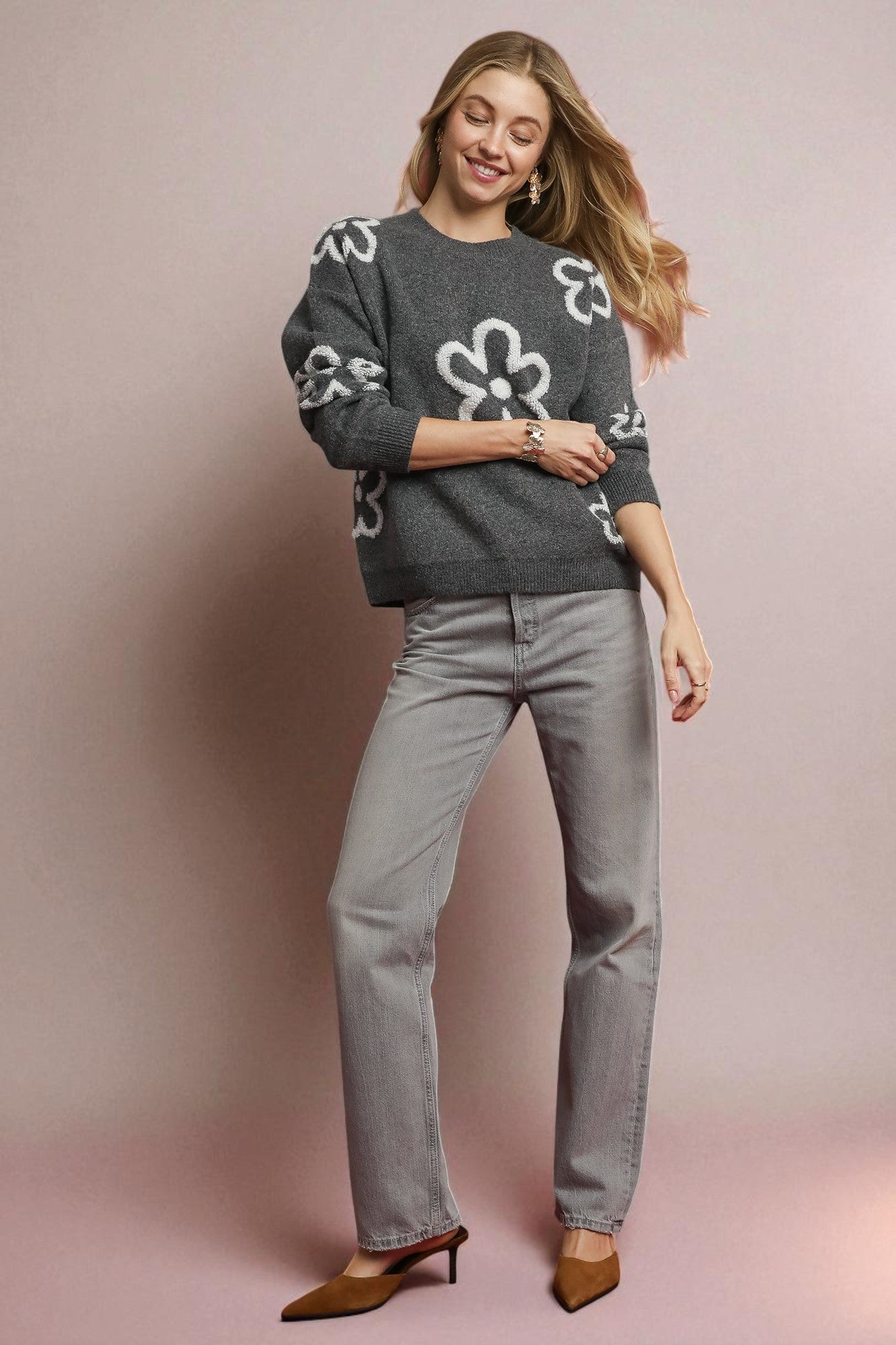 Woman wearing a gray sweater with floral patterns and gray jeans on a pink background