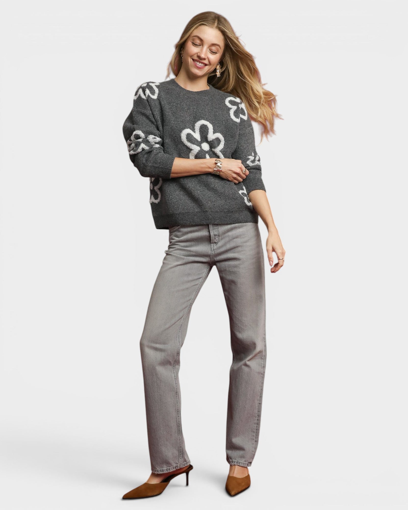 Woman wearing a gray sweater with white floral patterns and gray pants on a white background