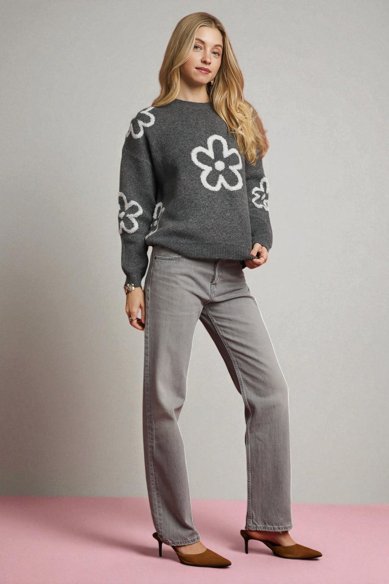 Woman wearing a gray sweater with white floral patterns and gray pants on a plain background