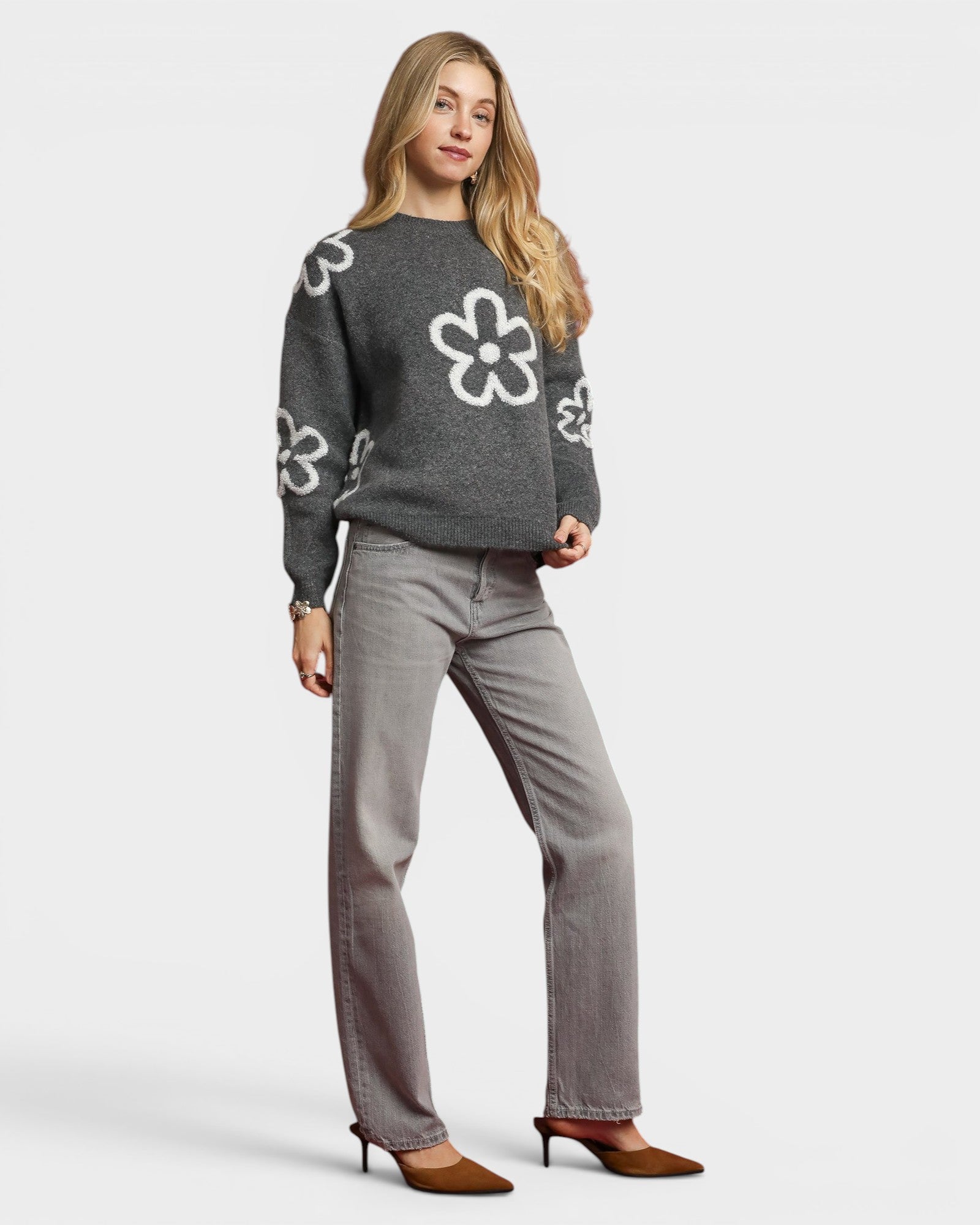 Woman wearing a gray sweater with white floral patterns and gray pants on a light gray background