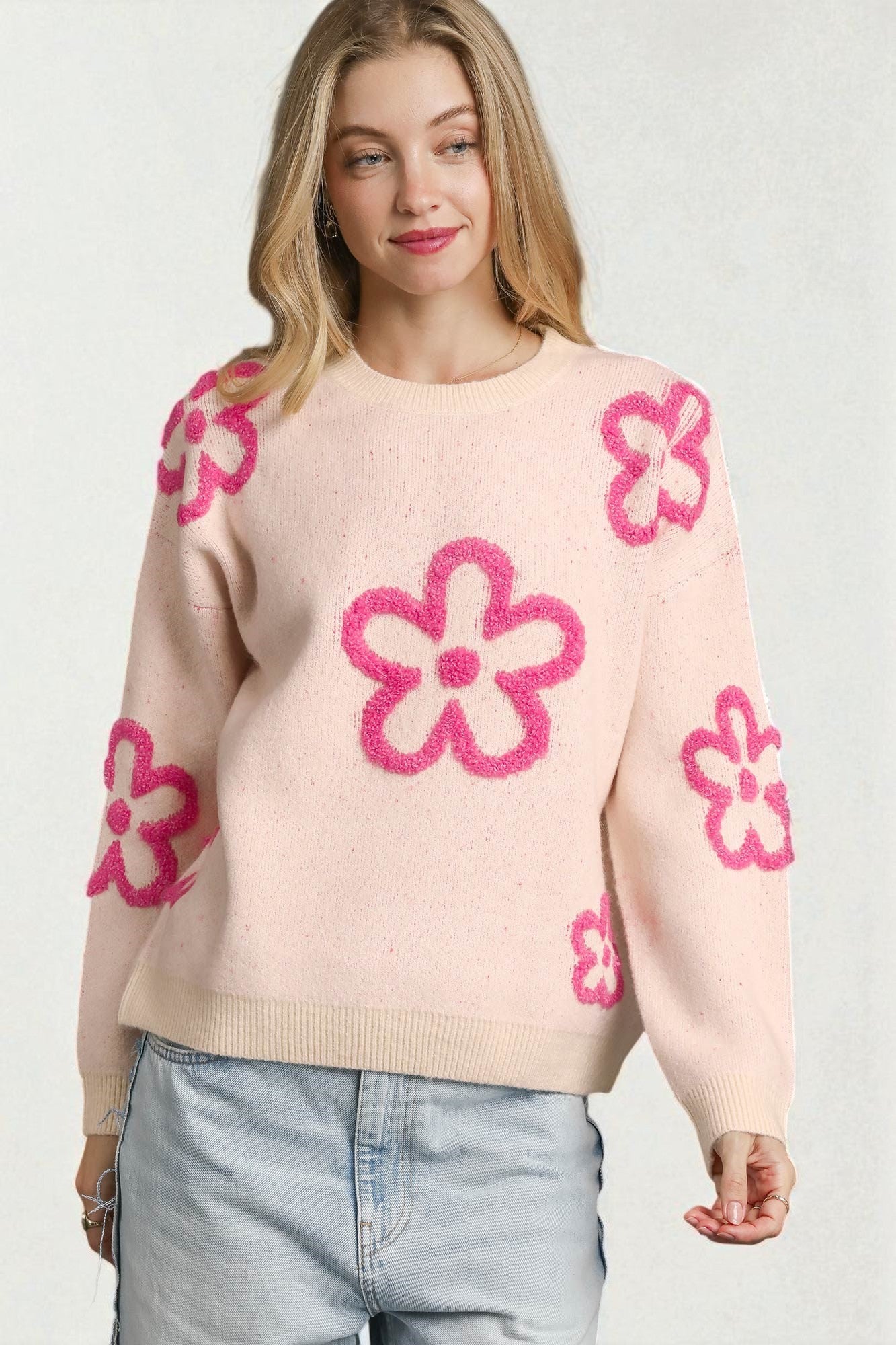 Woman wearing a light pink sweater with pink floral patterns on a white background