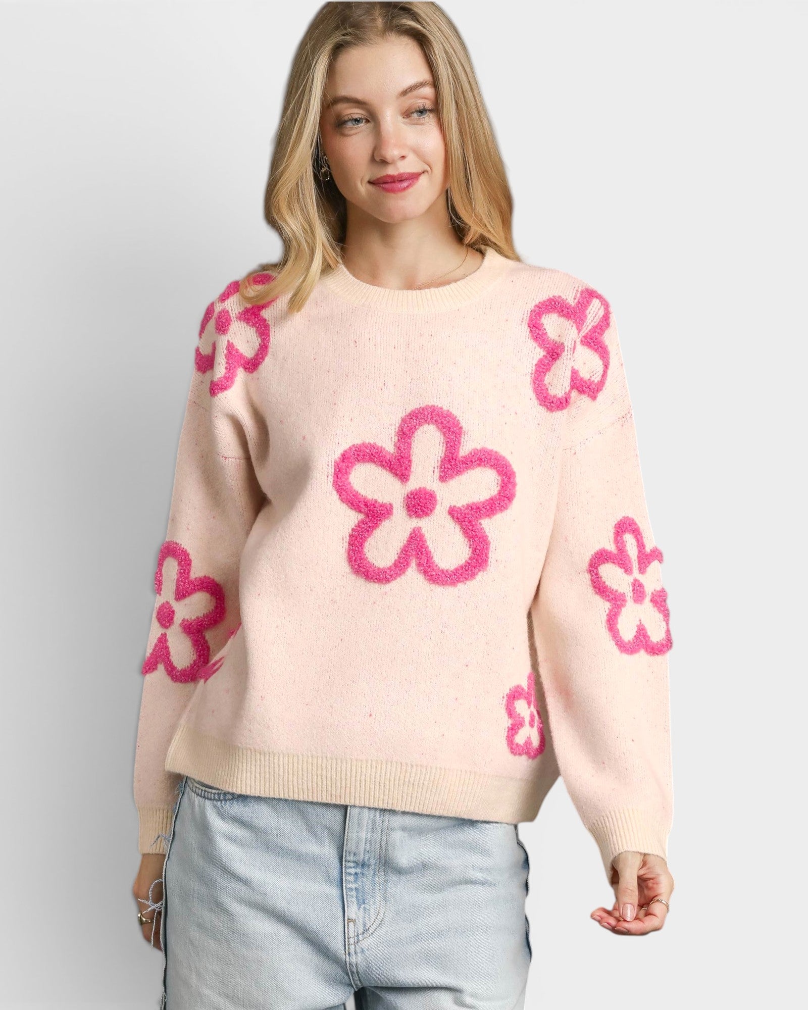 Woman wearing a light pink sweater with pink floral patterns on a plain background