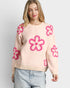 Woman wearing a light pink sweater with pink floral patterns on a plain background
