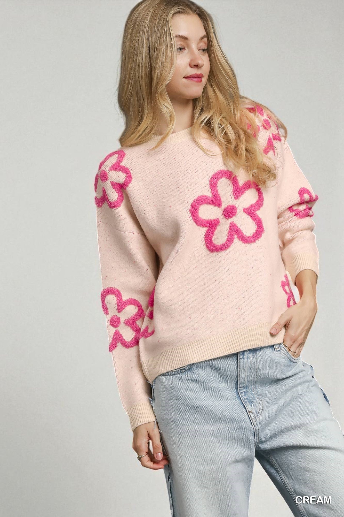 Woman wearing a cream sweater with pink floral patterns on a gray background