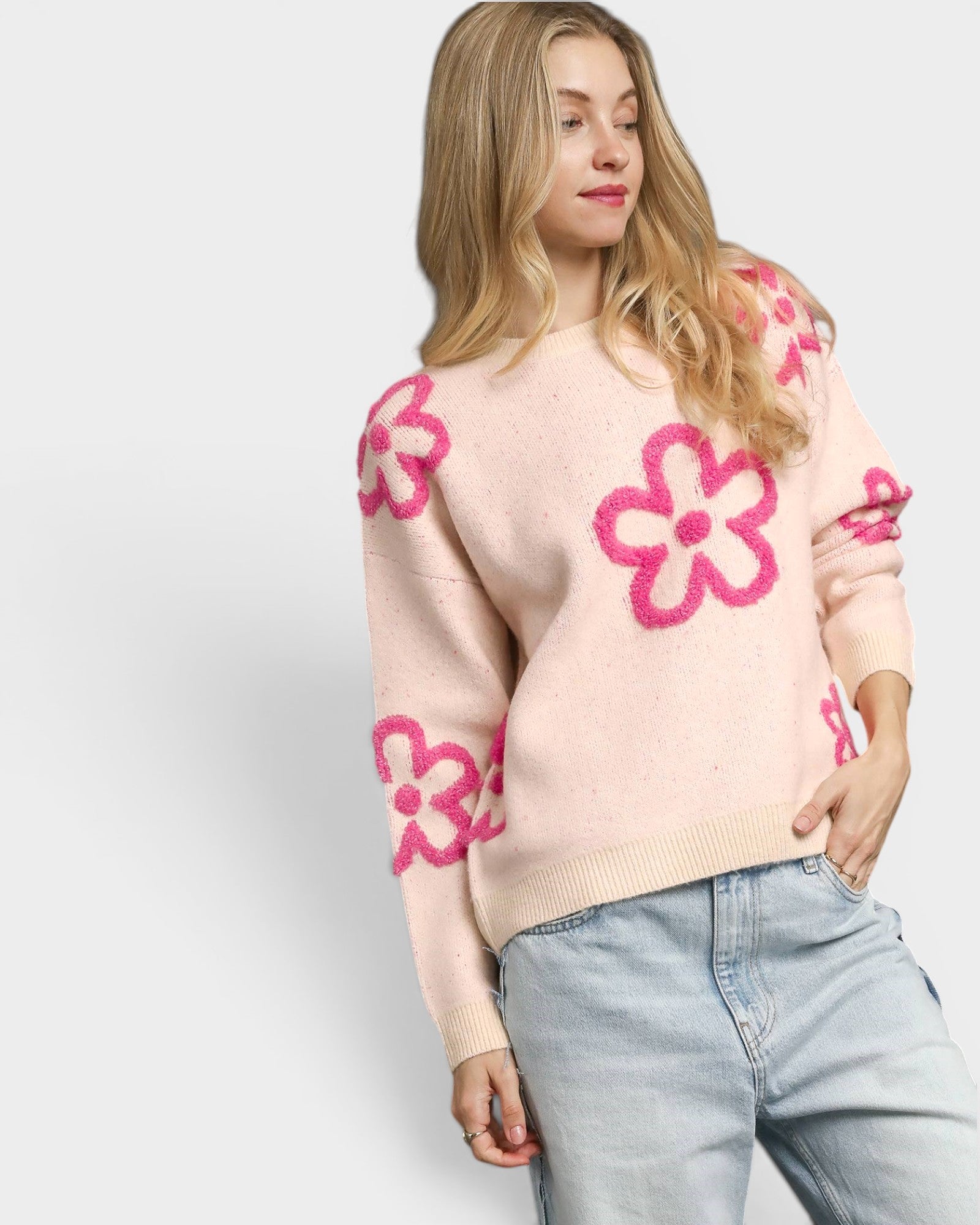 Woman wearing a light pink sweater with pink floral patterns on a plain background