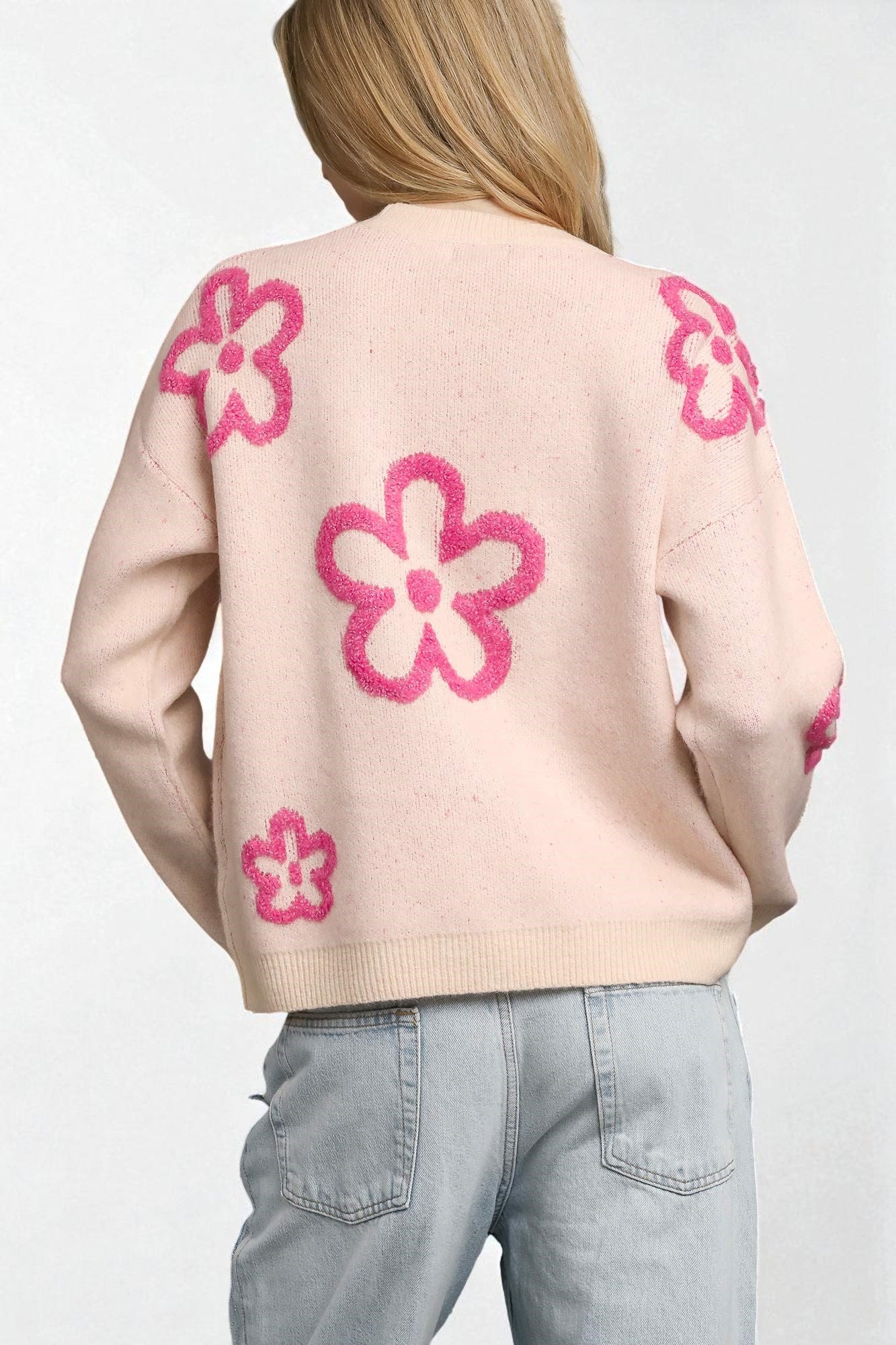 Person wearing a light pink sweater with pink floral patterns on a plain background