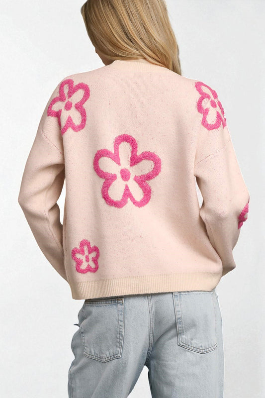 Person wearing a light pink sweater with pink floral patterns on a plain background
