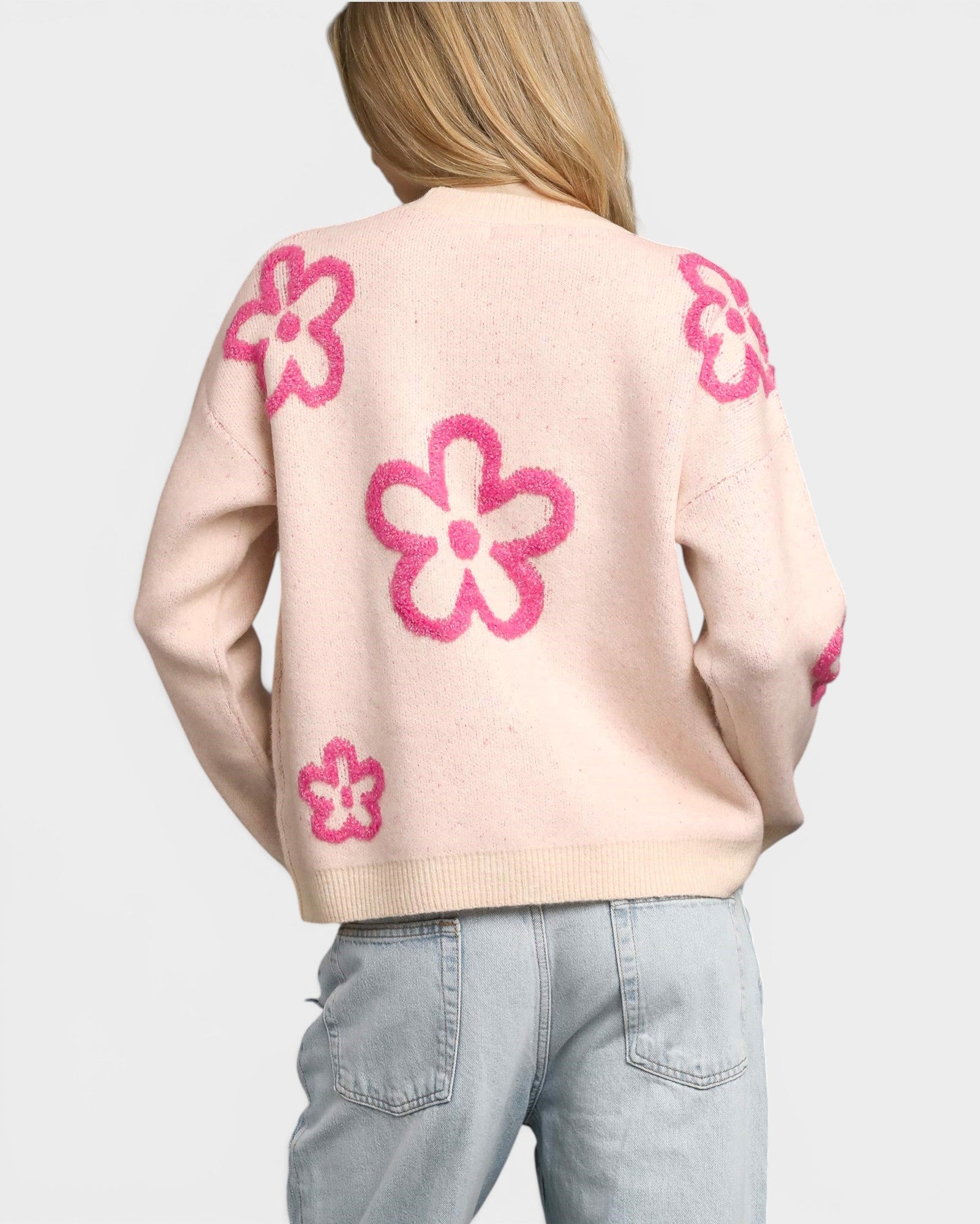 Woman wearing a light pink sweater with pink floral patterns on a plain background