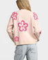 Woman wearing a light pink sweater with pink floral patterns on a plain background