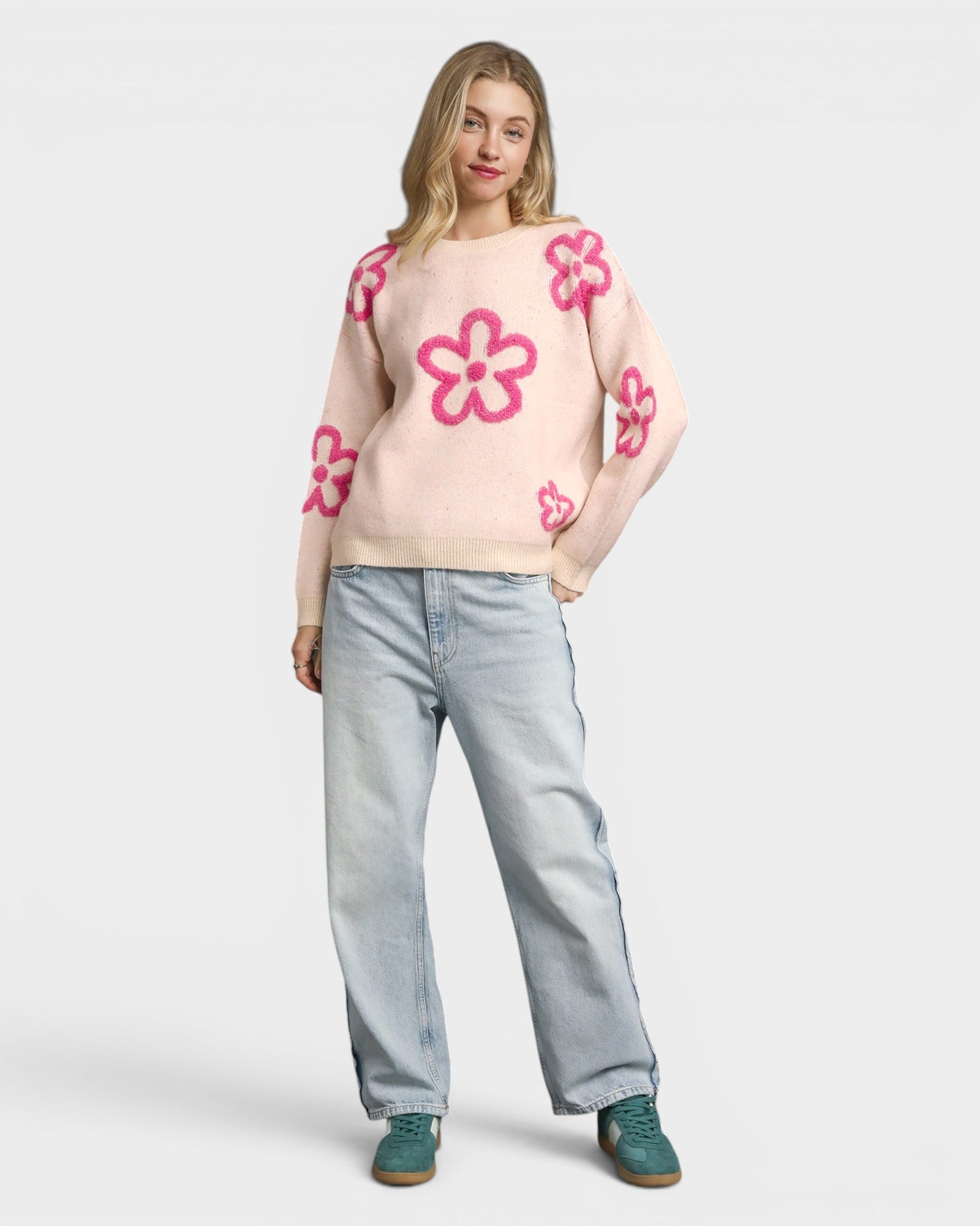 Woman wearing a light pink sweater with pink floral patterns and light blue jeans on a white background
