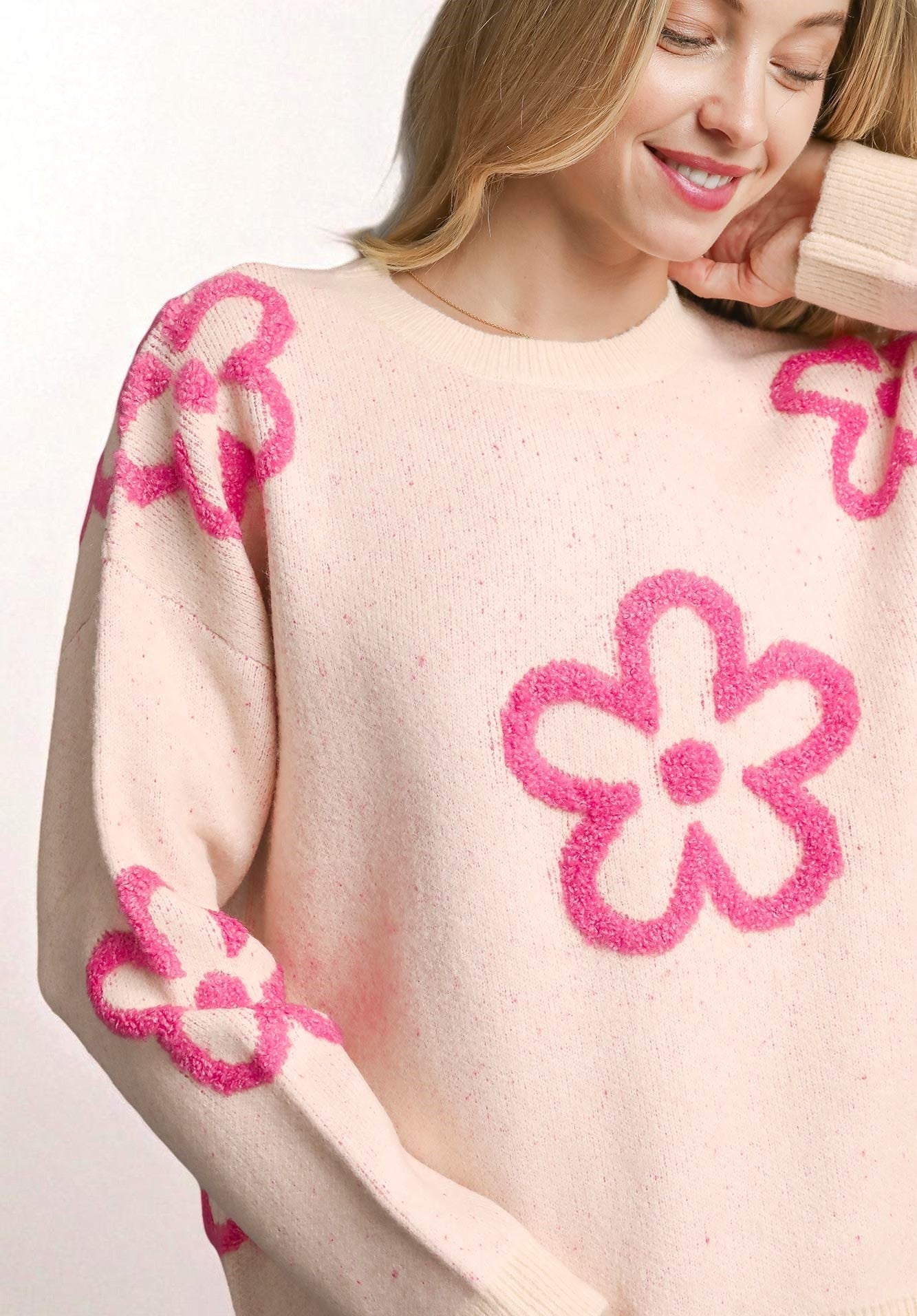Woman wearing a cream sweater with pink floral patterns on a white background
