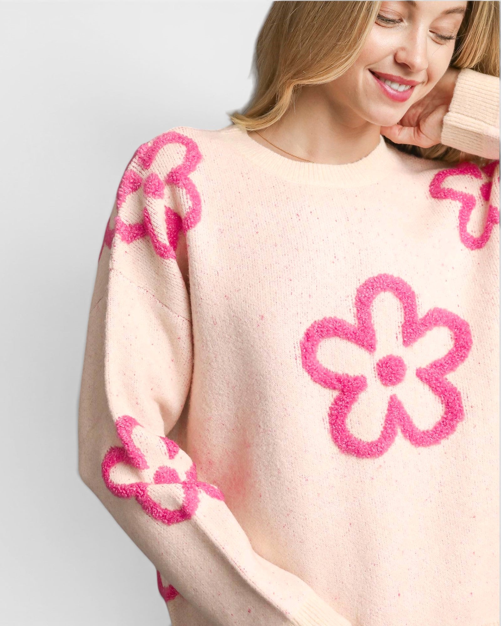 Woman wearing a sweater with pink floral patterns on a light background