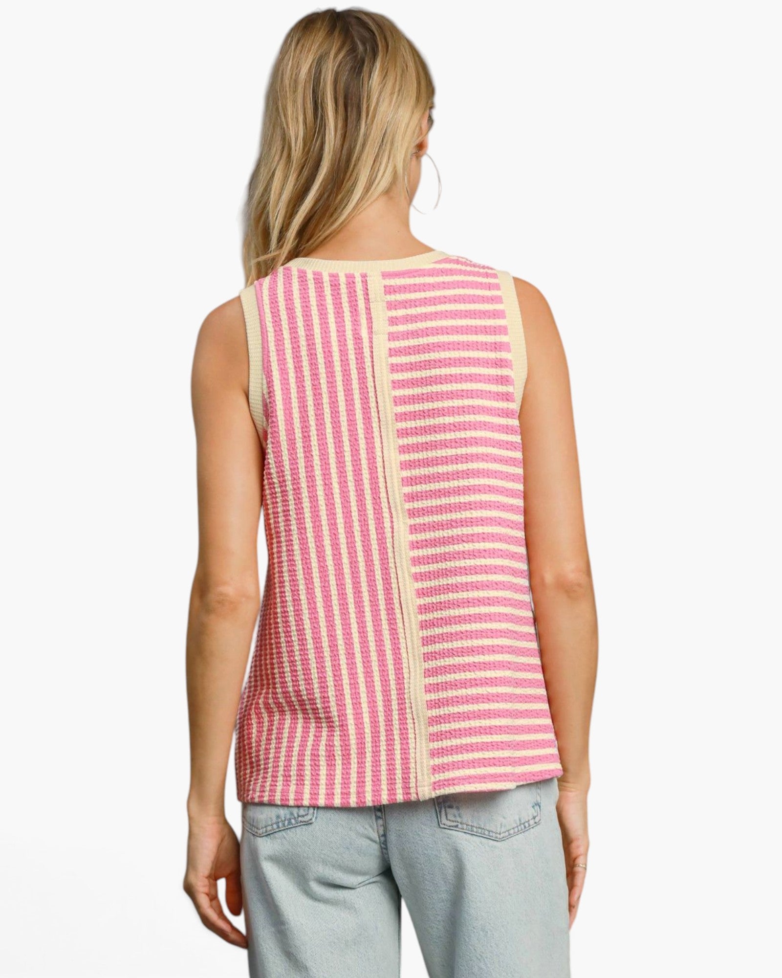 A woman shown from the back wearing a sleeveless knit top with vertical pink and cream stripes, paired with light-wash jeans, against a plain light gray studio background.