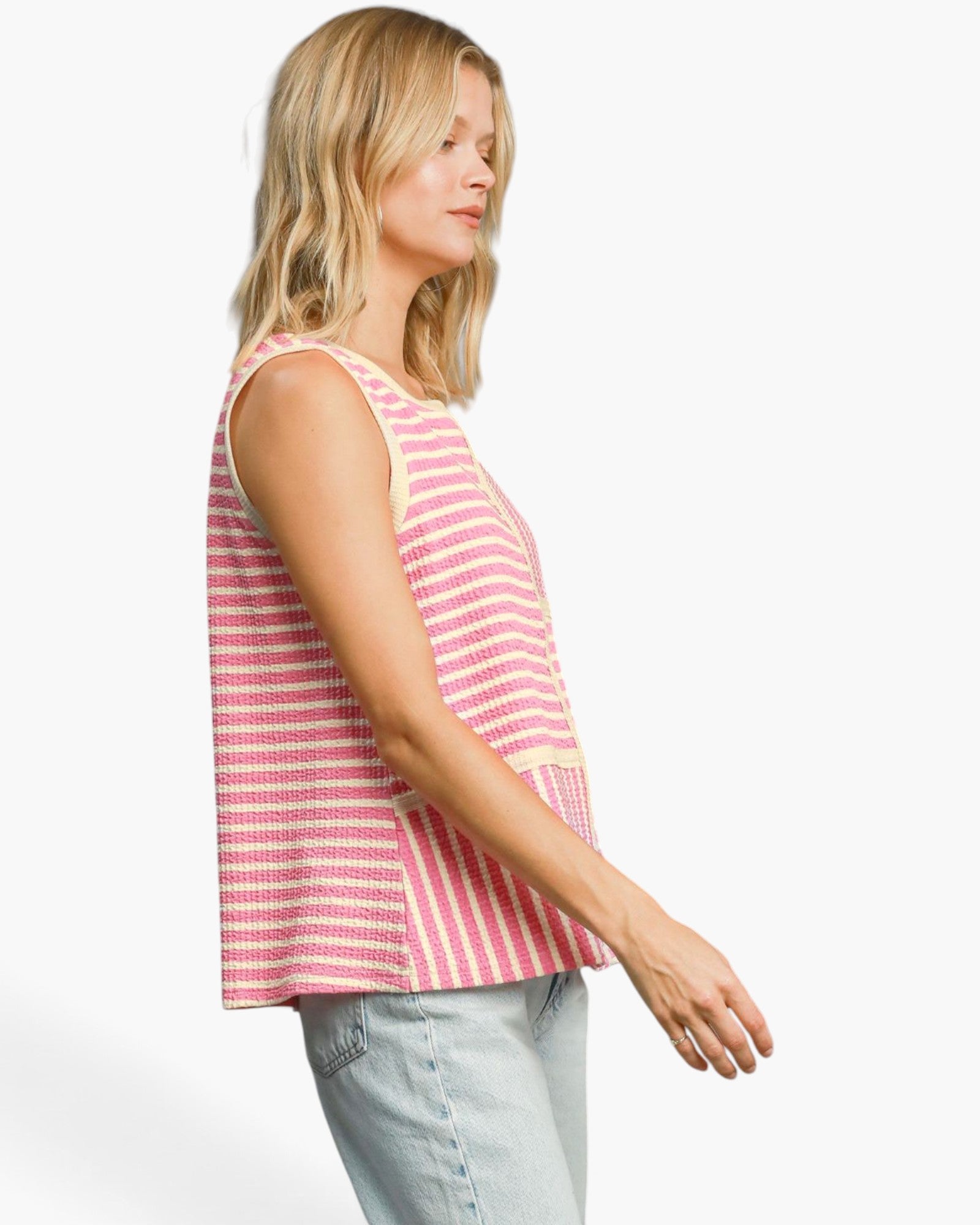 A woman shown in side profile wearing a sleeveless pink and white striped knit top with light blue jeans, photographed against a clean white studio background.