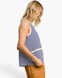 A woman shown from the side wearing a sleeveless knit top with blue and cream horizontal stripes, paired with tan pants, against a plain white studio background.