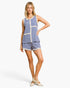 A woman modeling a sleeveless blue and white striped romper with cream trim, paired with matching striped shorts and cream heels, against a light gray studio background.