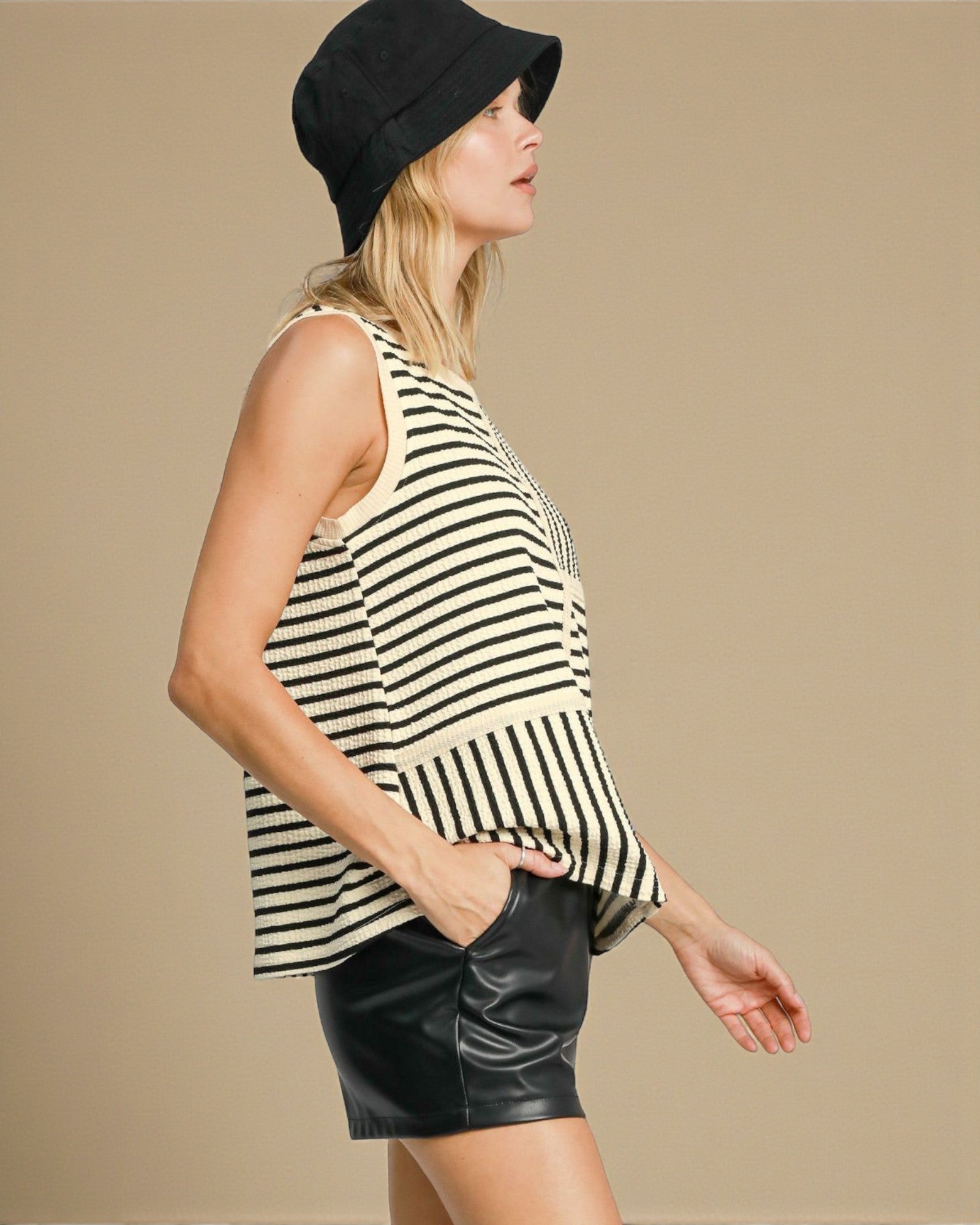 Woman wearing a black and white striped sleeveless top and black shorts on a beige background