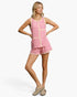 A woman modeling a pink and white striped sleeveless romper with beige trim, paired with beige flat shoes, against a light gray studio background.