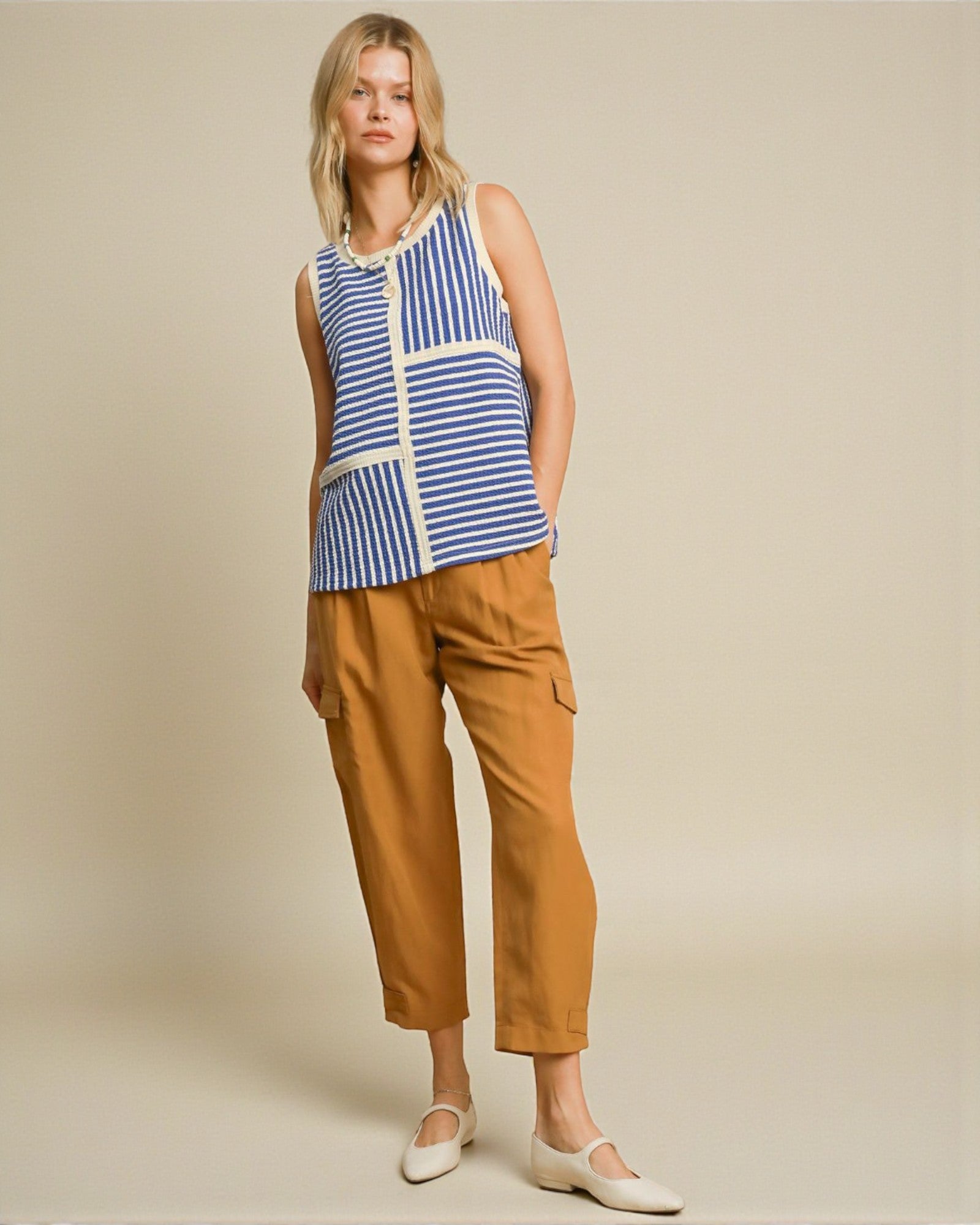 Woman wearing a blue and white striped sleeveless top with brown pants on a beige background