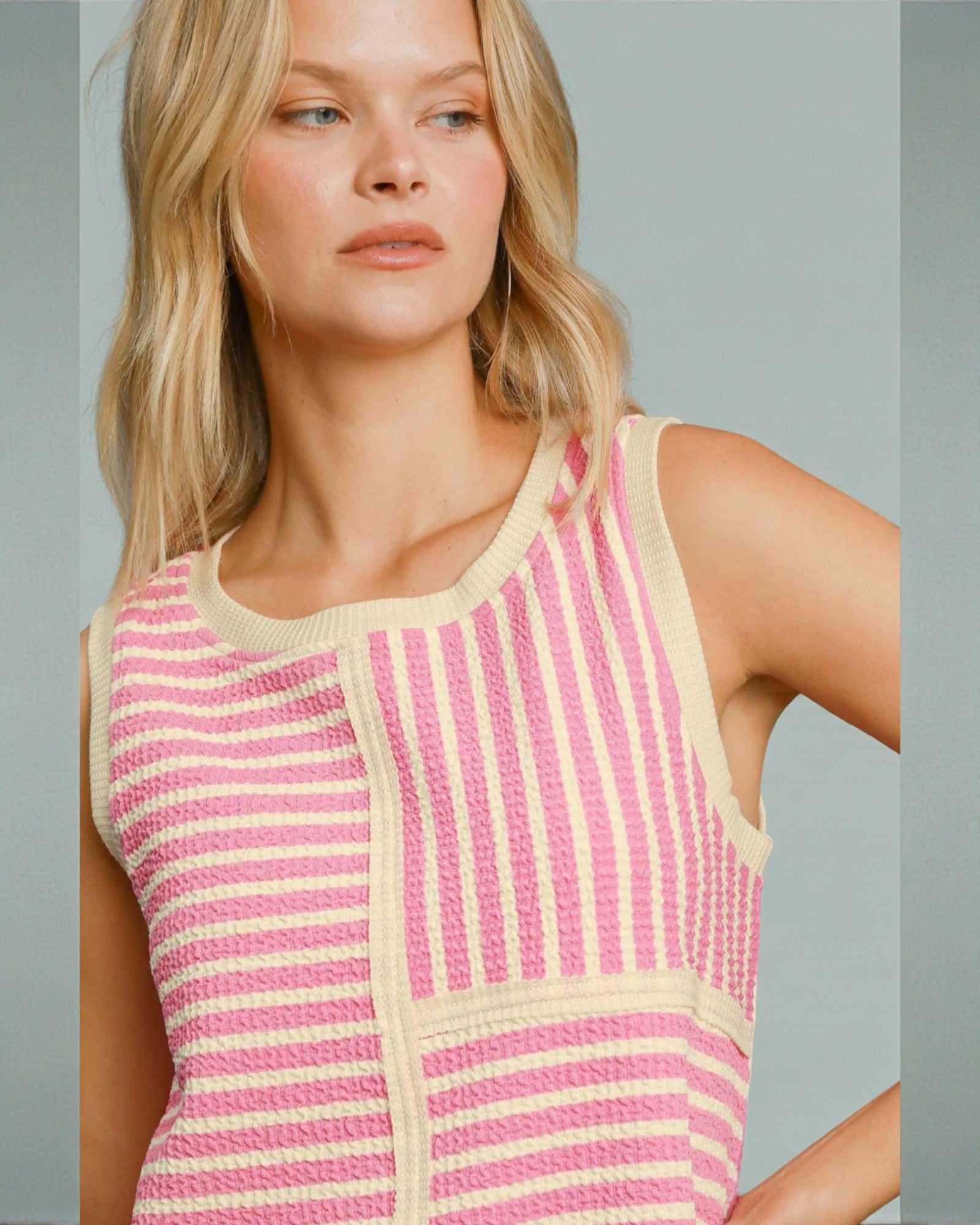 Woman wearing a pink and beige striped sleeveless top against a gray background