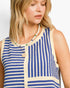 A close-up of a woman wearing a sleeveless knit top with vertical blue and cream stripes, paired with a beaded necklace, against a plain light background.