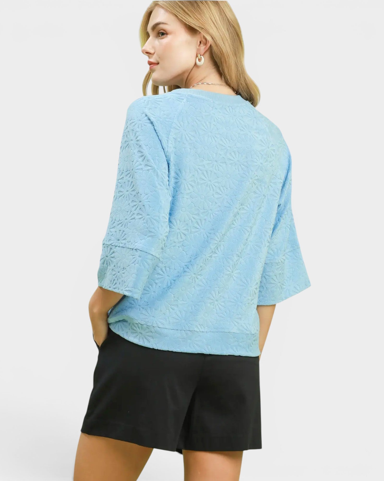 Woman wearing a light blue textured top and black shorts on a white background