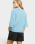 Woman wearing a light blue textured top and black shorts on a white background