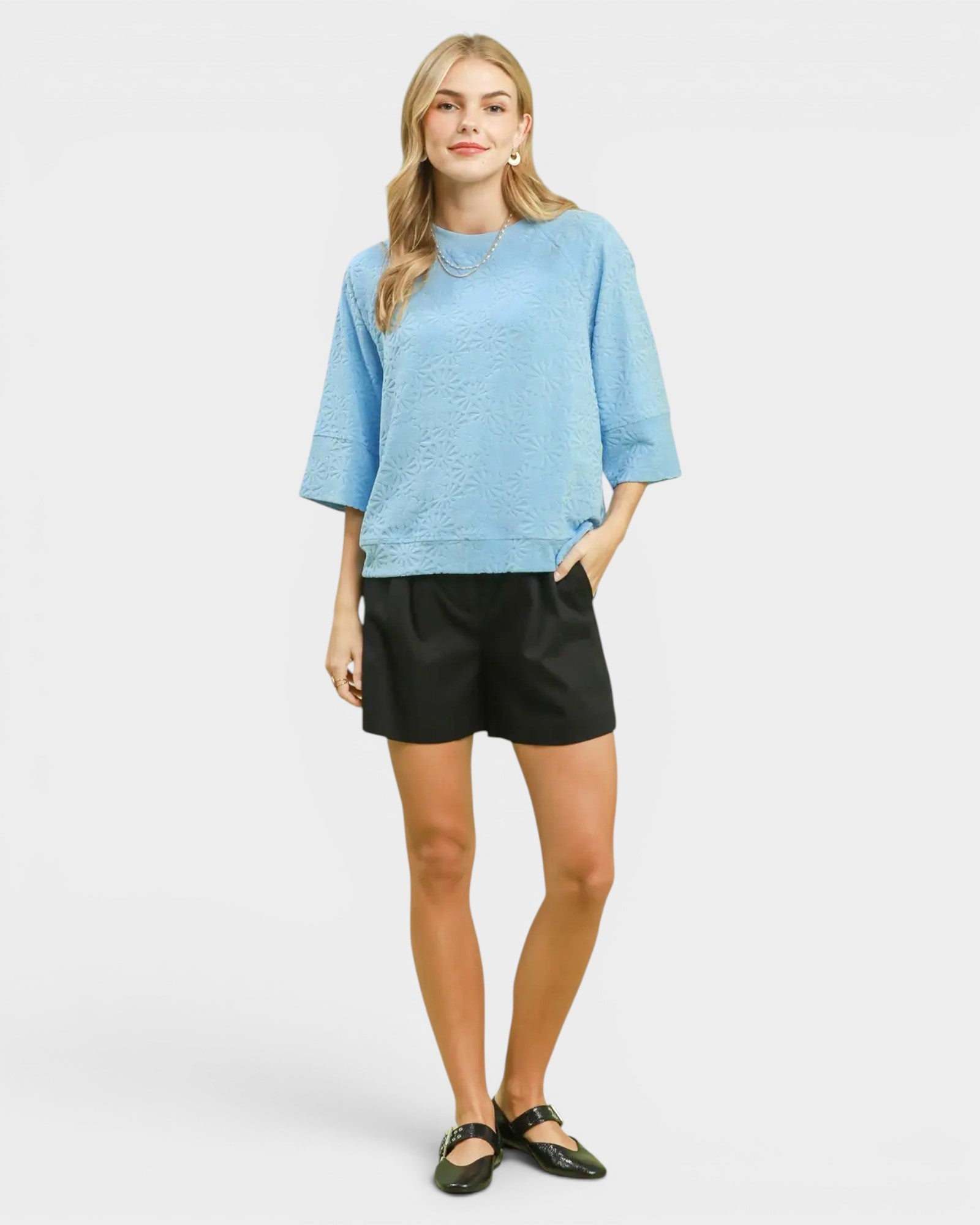 Woman wearing a light blue top and black shorts on a white background