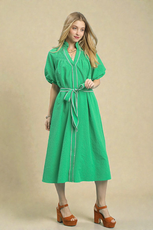 Woman wearing a green dress with a belt against a beige background