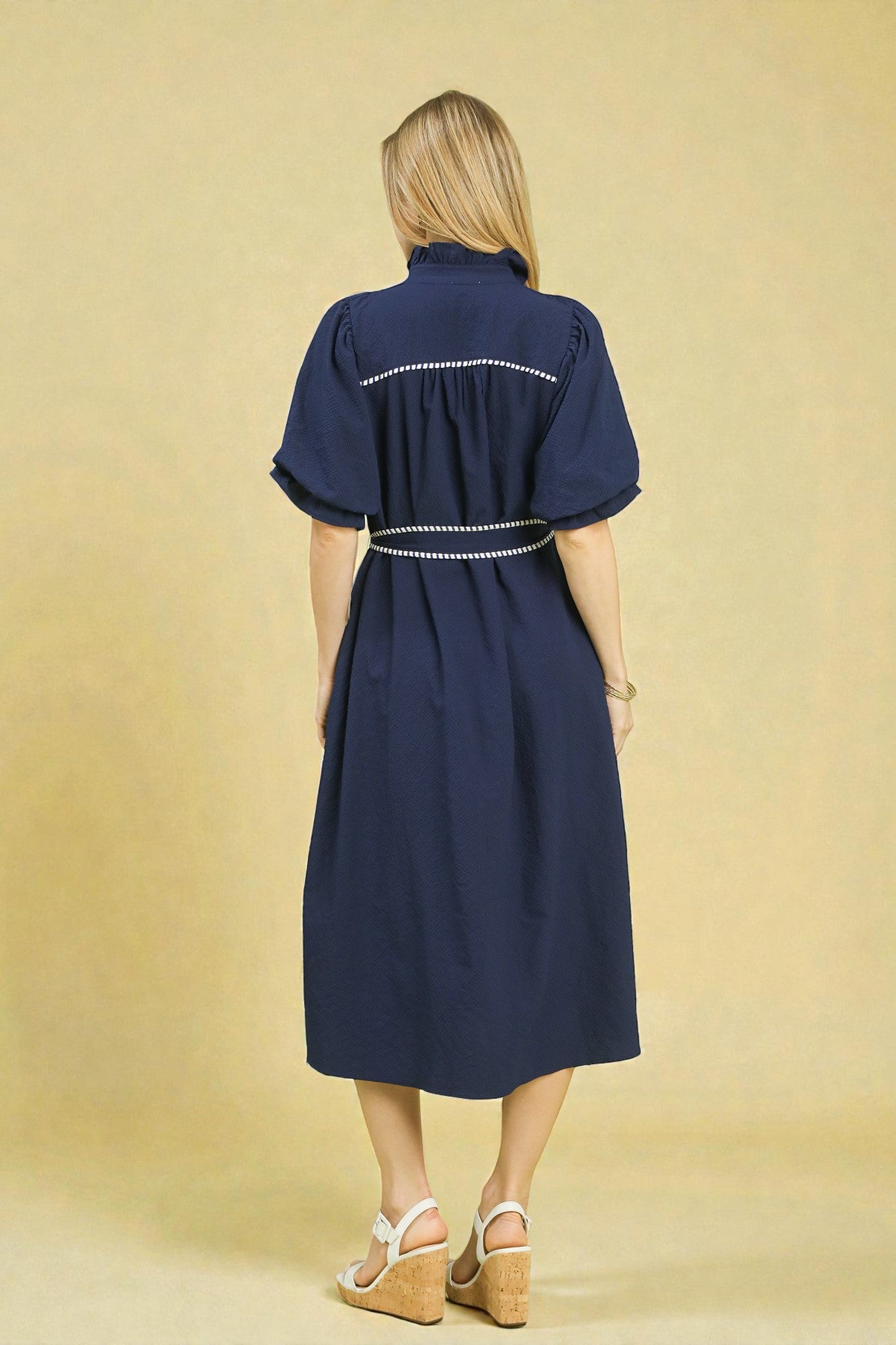 Woman wearing a navy dress with white trim on a beige background