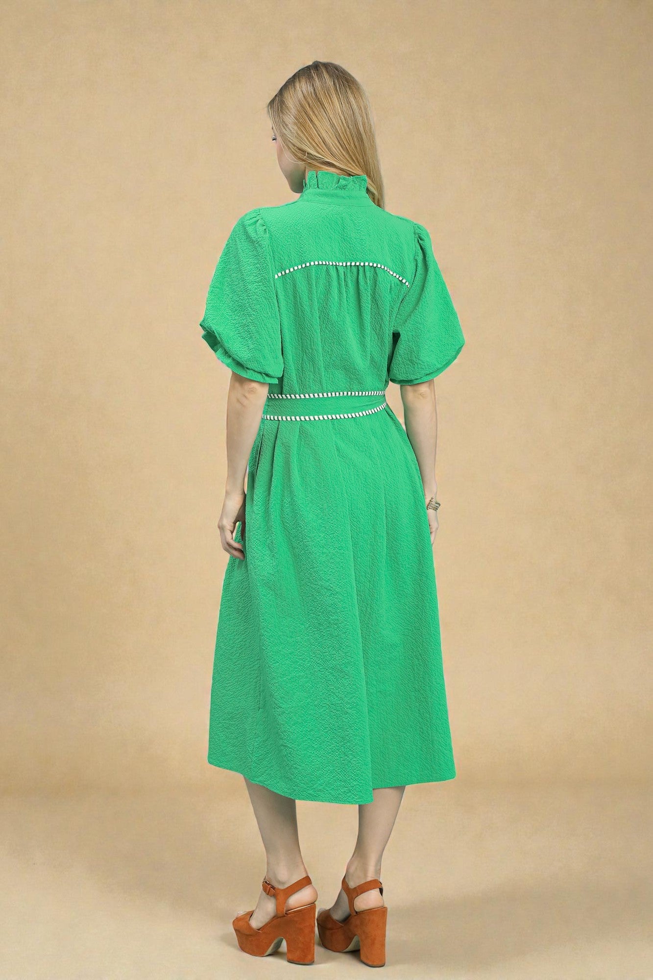 Woman wearing a green dress with white embroidery on a beige background