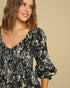 Woman wearing a black floral dress against a beige background