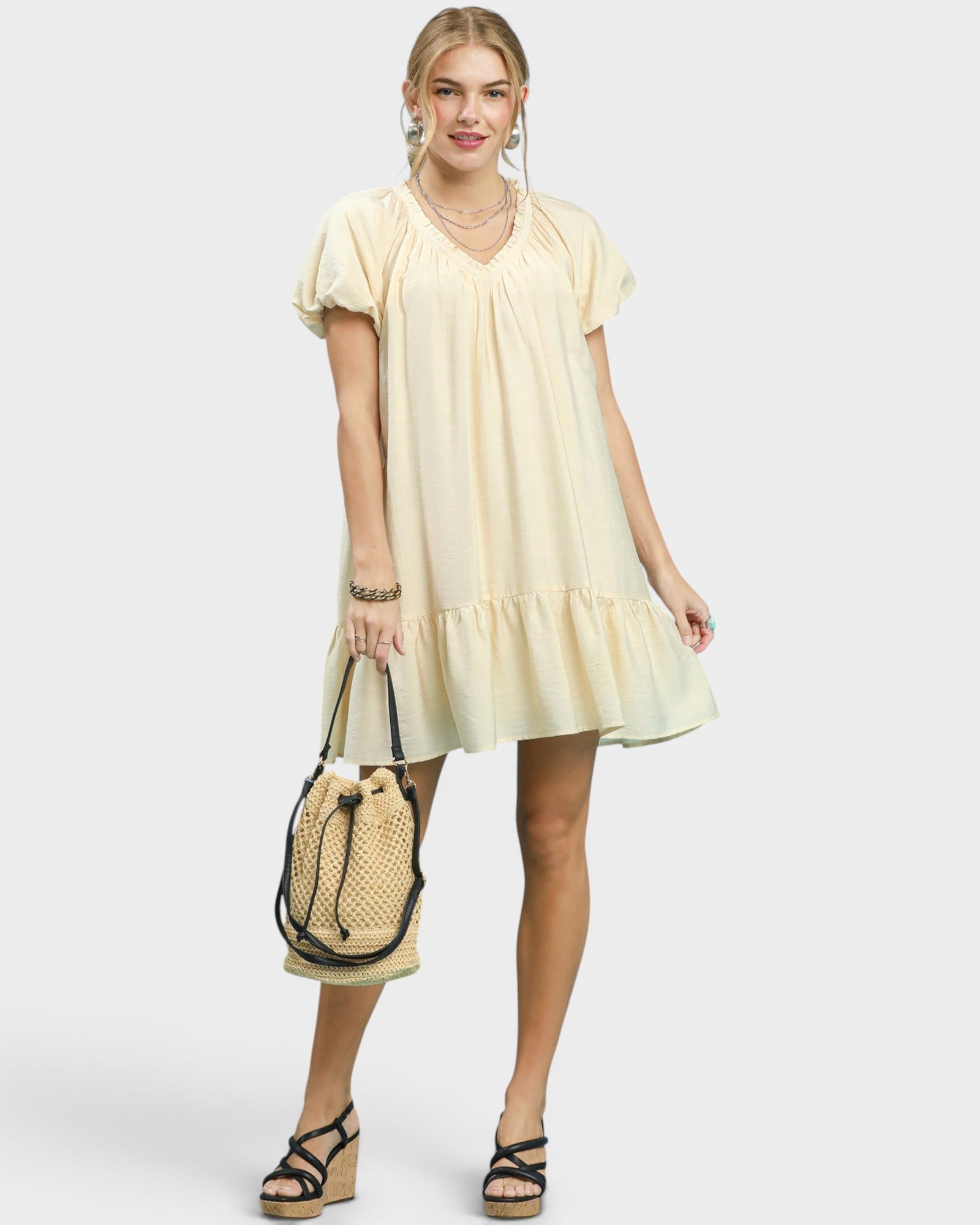 Woman wearing a light yellow dress holding a straw bag on a white background
