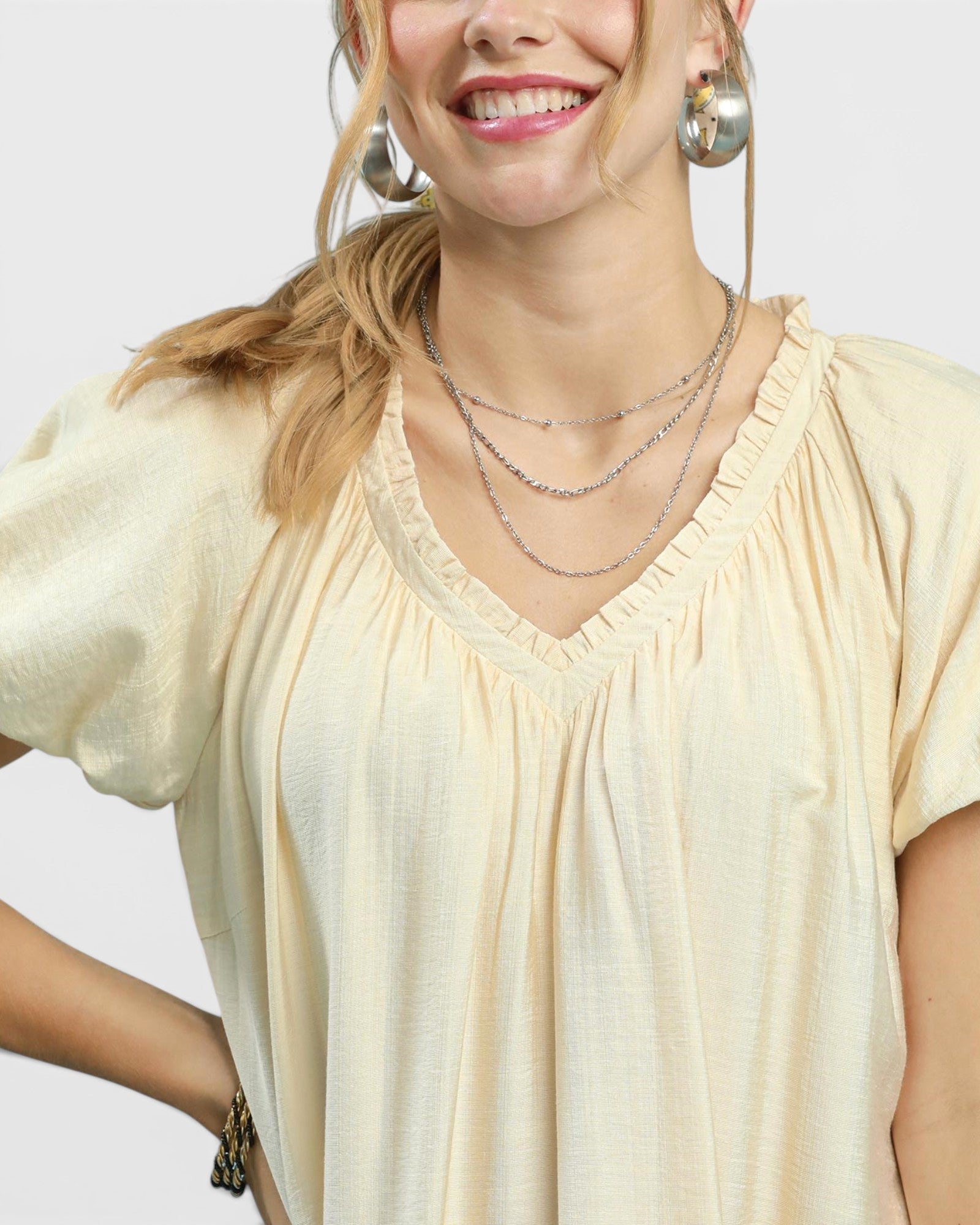 Woman wearing a light-colored blouse with layered necklaces on a plain background