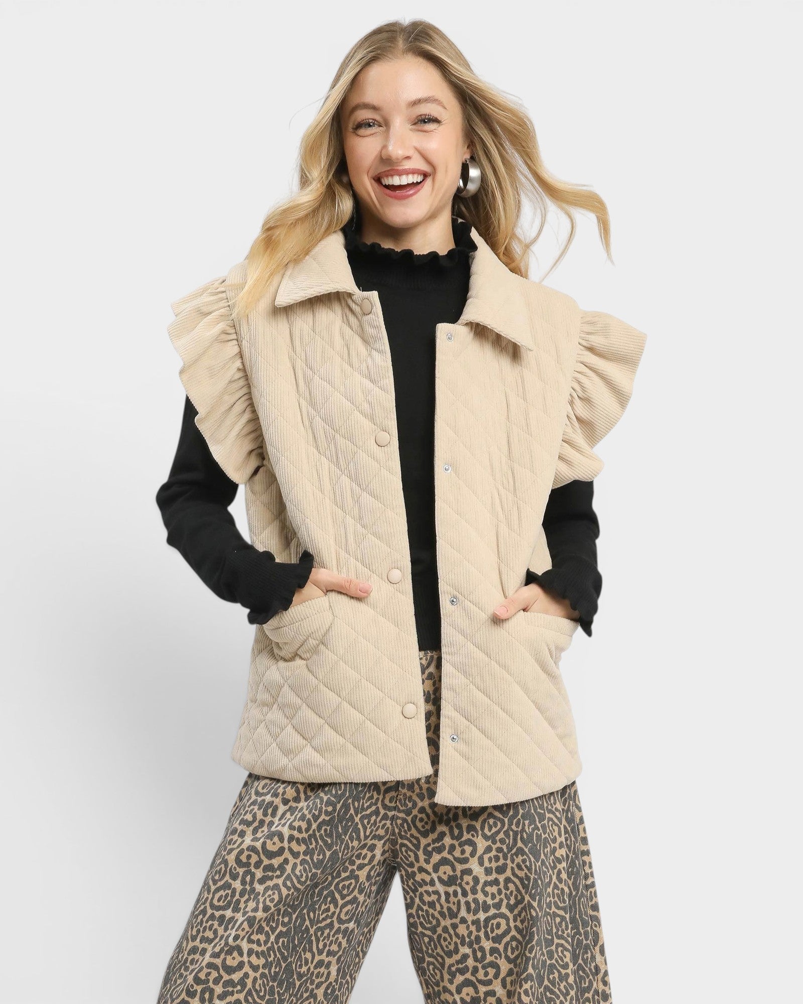Woman wearing a beige quilted vest over a black top with a white background
